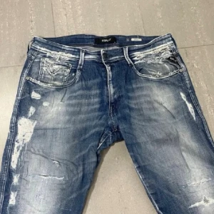 Replay jeans  - Säljer ett par blå jeans från Replay med slitningar och distressed detaljer. Jeansen har raka ben, klassisk femficksmodell och tydliga tvättade partier för en cool, avslappnad look. Perfekta för dig som gillar streetwear och trendig stil.