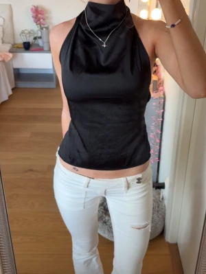 Svart halterneck topp med öppen rygg - Säljer en svart halterneck topp med hög krage och öppen rygg. Toppen knyts i nacken och har en croppad passform som visar midjan. 