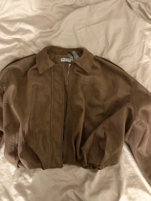 Brun skinnjacka från Meet Me There - Snygg brun skinnjacka från Meet Me There i modellen Miami Jacket. Jackan har klassisk krage, dragkedja framtill och en avslappnad passform. Perfekt för dig som gillar stilrena och tidlösa plagg. Märkt med storlek XXS/XS.