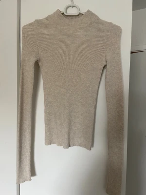 Beige ribbad stickad polotopp Gina Tricot - Säljer en beige ribbad stickad tröja från Gina Tricot. Tröjan har lång ärm, hög hals och är figurnära i modellen. 