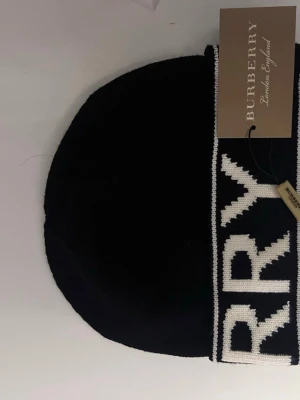 Svart mössa från Burberry - Snygg svart mössa från Burberry med bred vit logotyptext runt om den har aldrig använt den så den är helt ny