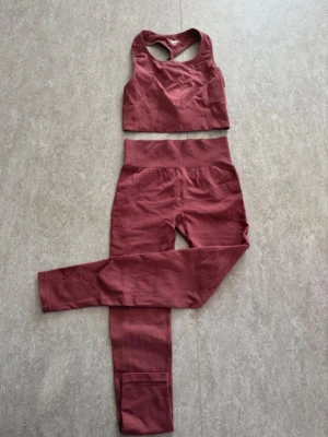 Träningsset - Ett vinrött(?) träningsset från Lager 157 bestående av tights och en sport-bh i seamless-modell. Tightsen är i storlek Small och sport-bh:n är i storlek Medium. Plaggen är oanvända men tvättade. Materialet är mjukt och stretchigt