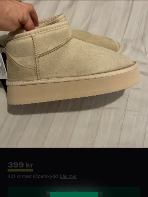 Beige fluffiga tofflor från Noya - Säljer ett par beige tofflor från Noya med mjuk, fluffig insida och hög platåsula. Utsidan är i mockaimitation och de har en enkel, stilren design med rund tå och låg ankel. Perfekta för att hålla fötterna varma hemma eller ute.