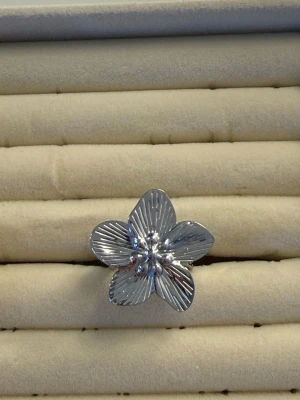 Silverfärgad blomring i metall - Snygg ring i silverfärgad metall formad som en blomma med fem blad. Blommans yta har räfflade detaljer som ger en cool och unik look. Perfekt accessoar för dig som vill sticka ut med något annorlunda och trendigt.