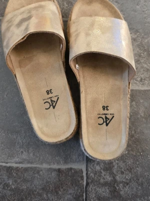Beige platåsandaler från AC - Säljer ett par snygga beige platåsandaler från AC Ann Christine. Sandalerna har breda remmar i skimrande material och en flätad platåsula som ger extra höjd. Perfekta för en trendig och avslappnad sommarlook.