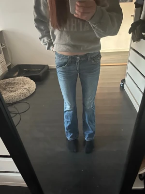 Blå bootcut jeans med låg midja - Säljer ett par klassiska blå bootcut jeans med låg midja och slitningar framtill. Jeansen har fem fickor och stängs med dragkedja och knapp. Perfekta för en avslappnad och trendig look. Pris kan diskuteras!❤️