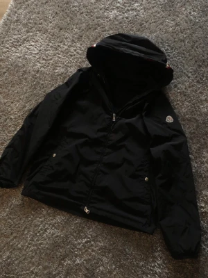 Moncler Jacka - Snygg svart vindjacka från Moncler med huva, Säljer den pågrund av att den är lite stor på mig och används inte så mycket och vill hellre sälja o köp nå annat plagg iställe.Den är i super bra skick och har inga skador, Den är storlek 5/L hör av er vid intresse💪🙏🏼Pris ej hugget i sten