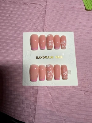 Rosa press-on naglar med blommor - Snygga press-on naglar i ljusrosa med subtila vita blommönster och rosa tippar. Naglarna har en mjukt fyrkantig form och ger en fräsch och trendig look. Perfekta för dig som vill ha en söt och stilren manikyr utan att gå till salong.