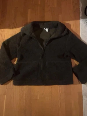 Mörkgrön teddyjacka - Mysig grön teddyjacka med dragkedja framtill och två stora fickor. Jackan har en hög krage och är gjord i fluffigt, mjukt material som håller dig varm. Perfekt för kyliga dagar och enkel att matcha med olika outfits.