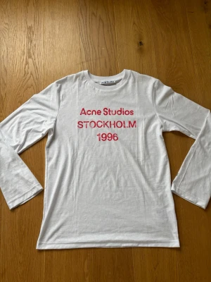 Vit långärmad Acne Studios t-shirt - Hej 👋 Vit långärmad t-shirt från Acne Studios med röd text 'Acne Studios STOCKHOLM 1996'. Tröjan har inga defekter! Är oversized i storleken 