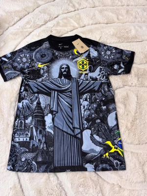 Nike Brasil T shirt - Unik svart t-shirt från Nike med grafiskt tryck av Kristusstatyn och brasilianska motiv. T-shirten har korta ärmar, rund hals och detaljer i gult, grönt och blått. Perfekt för dig som vill sticka ut med en cool streetwear-look. 