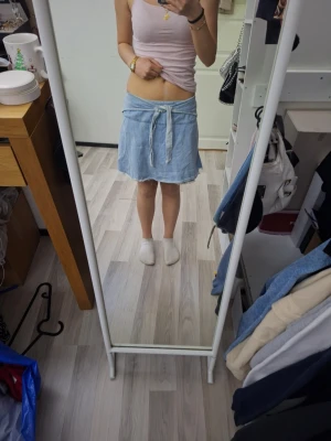 Ljusblå kortkjol med knytband - Säljer en ljusblå kortkjol i mjukt material med knytband i midjan och avslappnad passform. Kjolen har som typ shorts under så den inte ska kunna blåsa upp, men det syns inte. Kjolen har en enkel design och är perfekt för varmare dagar. Passar dig som gillar en chill och bekväm stil.