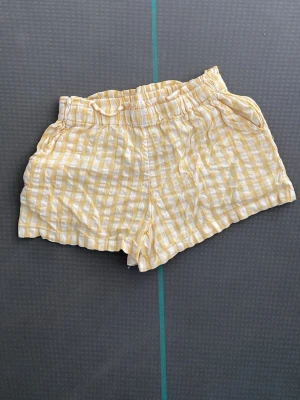 Gulvitrandiga shorts med resårmidja - Säljer ett par somriga shorts med gulvita ränder och skön resår i midjan. De har en avslappnad passform och är tillverkade i ett lätt och luftigt tyg, perfekta för varma dagar.