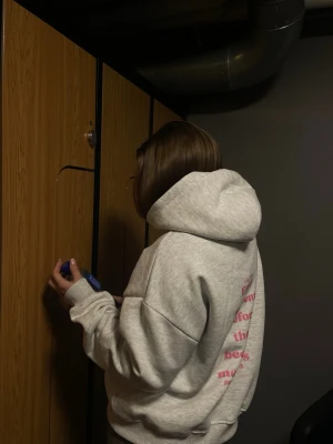 Grå hoodie med rosa text - Säljer en oversized grå hoodie med stor huva och tryck i rosa text på ryggen. Hoodien har en avslappnad passform och är tillverkad i mjukt sweatshirtmaterial, perfekt för en chill och casual look.  Märket står på framsida. Skicka för fler bilder.