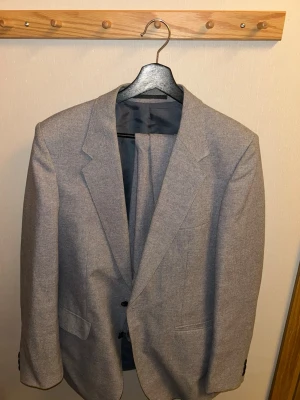 Ljusgrå kavaj med matchande byxor - Snygg ljusgrå kavaj med matchande byxor. Klassisk modell med två knappar framtill, fickor och slät insida i blankt tyg. Perfekt för dig som vill ha en stilren och enkel look. Passar till skjorta eller t-shirt för en clean outfit. Passar man 175-185cm och 72-82kg.