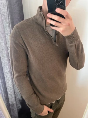Brun halvzip tröja från Bondelid - Säljer en stilren brun stickad tröja från Bondelid med halv dragkedja och hög krage. Tröjan har ribbade muddar vid ärmslut och nederkant, perfekt för en clean och avslappnad look. Storlek S