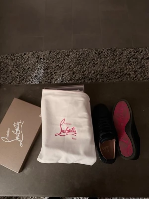 Christian Louboutin navy sneakers - Snygga mörkblå sneakers från Christian Louboutin med klassisk röd sula och diskret logga på insidan. Skorna har ovandel i mocka och läder, svarta skosnören och en stilren design som sticker ut med den ikoniska röda undersidan. Använda fåtal gånger. Box o dustbag medföljer!