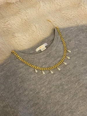 Guldfärgat halsband med pärldroppar - Snyggt halsband med guldfärgad kedja och hängande droppformade pärlor. Perfekt accessoar för att lyfta din outfit med en trendig och elegant touch. Kedjan har en klassisk design och pärlorna ger en extra detalj.