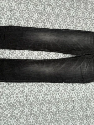Svarta slim fit jeans med slitningar Nudie jeans - Säljer ett par svarta slim fit jeans med diskreta slitningar och tvättade detaljer. Jeansen har klassisk femficksdesign och raka ben. Perfekta för dig som gillar en stilren och modern look.