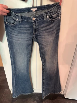 Blå bootcut jeans från Gina tricot  - Ett par blå bootcut jeans från Gina tricot  med klassisk femficksdesign och snygga slitningar framtill. Jeansen har låg midja, utsvängda ben och är gjorda i denim med lätt stretch för skön passform. Perfekta för en avslappnad och trendig look.