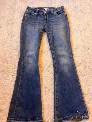 Blå bootcut jeans lågmidjade - Säljer ett par blå bootcut jeans med lätt slitna detaljer och fransad nedkant, från Gina i storlek S❤️har sprättat längst ner