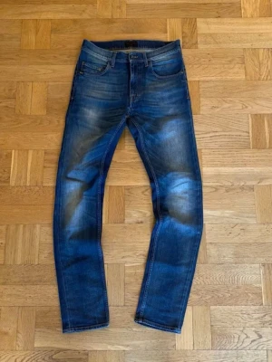 Blå slim fit jeans tiger of Sweden  - Snygga blå slim fit jeans med coola slitningar och faded detaljer på framsidan och baksidan. Knappt använd. Klassisk femficksdesign och normal midja. Perfekta för dig som gillar en modern och avslappnad look. Materialet är denim.