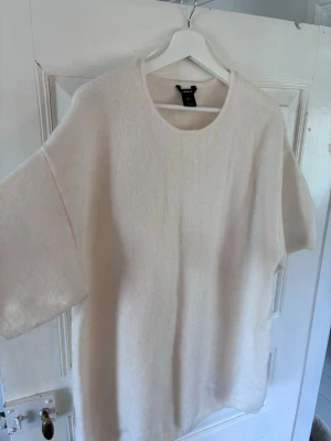 Krämvit stickad tröja från Lindex - Mysig krämvit stickad tröja från Lindex med rund halsringning och korta, vida ärmar. Tröjan har en avslappnad passform och är tillverkad i ett mjukt, fluffigt material som känns skönt mot huden. Perfekt för lager på lager och enkel att styla.