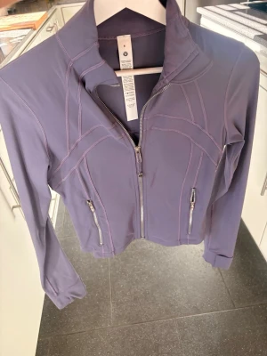 Lila zip-jacka från Lululemon - Snygg lila träningsjacka från Lululemon med figurnära passform, långa ärmar och dragkedja framtill. Jackan har två fickor med dragkedja och dekorativa sömmar. Perfekt för gymmet eller löprundan. Den har aldrig använts och är nu utan prislapp men prislapp finns som kan fås med. Storlek 6 som motsvarar 36/S. Nypris: 1380kr, Pris är diskuterbart🥰