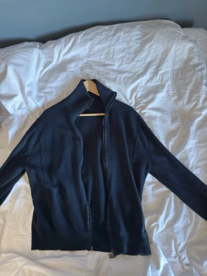 Mörkblå ziptröja från Massimo Dutti - Snygg mörkblå ziptröja från Massimo Dutti med hög krage och hel dragkedja. Tröjan har en stilren design och är tillverkad i ett mjukt, stickat material. Perfekt för lager-på-lager och enkel att matcha med olika outfits. Nypris:900 kr