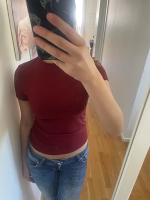 Mörkröd tight t-shirt H&M - En enkel och stilren mörkröd t-shirt med tight passform och korta ärmar. T-shirten har rund halsringning och är gjord i mjuk bomull, perfekt till jeans eller kjol. Snygg basic som funkar året runt.