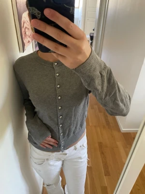 Grå kofta med pärlknappar - Snygg grå kofta med rund halsringning och pärlknappar hela vägen framtill. Långärmad och i mjukt, tunt stickat material. Perfekt att slänga över en t-shirt eller bära stängd för en clean look.