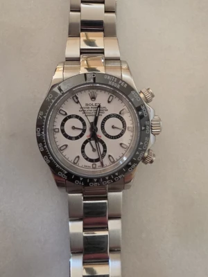 Panda Daytona silverfärgad klocka med svartvit urtavla - Säljer en stilren Daytona med silverfärgat armband i metall och svartvit urtavla. Klockan har tre mindre urtavlor, svart bezel med tachymeterskala och klassisk länkdesign. Perfekt för dig som gillar exklusiva klockor och tidlös design. Sveper vackert med automatisk mekanism, alltså inget batteri i. Länkar följer med, då jag har kortat ner. Säljes bara för att jag ska köpa en Daytona med grön urtavla.