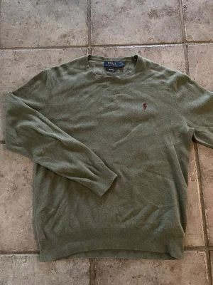 Olivgrön tröja från Polo Ralph Lauren - Olivgrön långärmad tröja från Polo Ralph Lauren i mjuk pima-bomull. Klassisk rund halsringning och diskret broderad logga på bröstet. Perfekt för en stilren och avslappnad look.