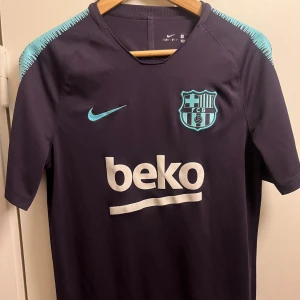 Nike FC Barcelona - Snygg Lila FC Barcelona tröja från Nike med korta ärmar och turkosa detaljer. Tröjan har klubbens emblem och sponsorlogga på framsidan. Perfekt för fans som vill visa sitt stöd med stil! 💙