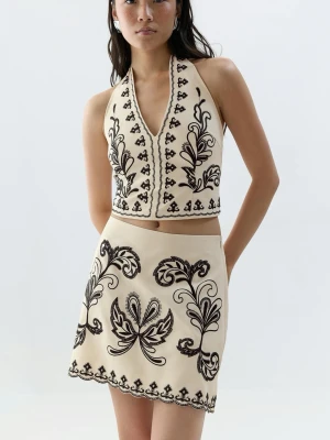 Beige broderat set med kjol och topp - Snyggt tvådelat set i beige med svart broderi från Gina Tricot. Toppen har halterneck och djup V-ringning, medan kjolen är kort och A-linjeformad. Setet har dekorativa broderade mönster och vågig kant. Aldrig använt!!!💘