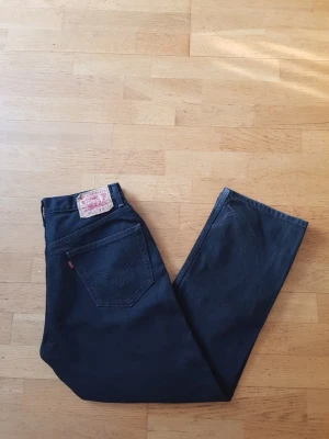 Svarta Levi's 505 jeans - Säljer ett par svarta Levi's 505 jeans med klassisk femficksdesign och rak passform. Jeansen har den ikoniska läderpatchen bak i midjan och röd Levi's-tagg på bakfickan. Perfekta för dig som gillar en tidlös och clean look.