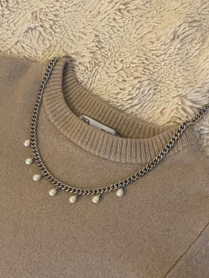 Silverfärgat halsband med pärlor från Zara - Snyggt halsband i silverfärgad rostfritt med kedja och små vita pärlor som hänger längs hela framsidan. Perfekt accessoar för att lyfta din outfit med en trendig och elegant touch. Passar till många olika stilar och är lätt att matcha.