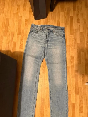 Ljusblå raka jeans från Levi's - Säljer ett par klassiska ljusblå jeans från Levi's med rak passform och fem fickor. Jeansen har en vintagekänsla med diskret tvätt och Levi's ikoniska läderpatch bak i midjan. Perfekta för en avslappnad och stilren look.