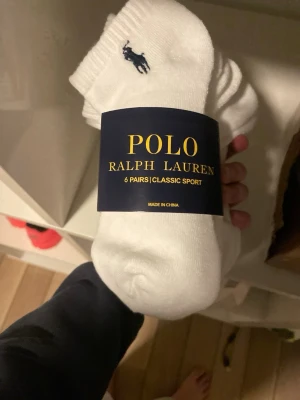 Vita sportstrumpor Polo Ralph Lauren - Säljer ett 6-pack klassiska vita sportstrumpor från Polo Ralph Lauren. Strumporna har den ikoniska mörkblå loggan broderad vid ankeln och är tillverkade i mjuk bomullsmix för skön passform. Perfekta till sneakers och vardagsstil.