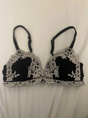 Intimissimi bh - Snygg svart bh med vit spetsbrodyr och justerbara axelband. Bh:n har dekorativa spetsdetaljer både fram och bak samt hakknäppning i ryggen. Materialet är mjukt och stretchigt för extra komfort.