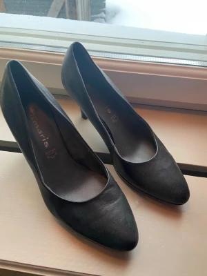 Svarta mockapumps från Tamaris - Snygga svarta pumps från Tamaris i mockaimitation med spetsig tå och smal klack. Klassisk och stilren modell som ger en elegant look. Insidan är mjuk och bekväm, perfekt till dig som gillar tidlös design. Köpta på sellpy för 80kr