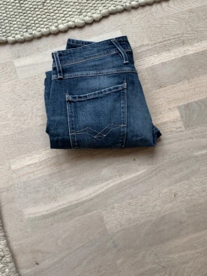 Replay anbass - Säljer ett par blå jeans med raka ben och snygga slitningar. Jeansen har klassiska fem fickor och kontrastsömmar. Perfekta till en avslappnad stil och passar till det mesta. Materialet är denim i bomull storlek 33/34 men uppsydda så längd topp till tå är 91/92 cm.