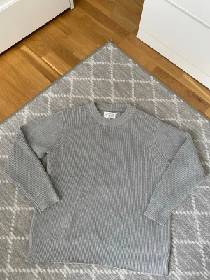 Maison Margiela Sweater - Snygg grå stickad tröja från Maison Margiela med rund halsringning och ribbade muddar. Tröjan har en klassisk rak passform och är tillverkad i ett mjukt, tjockt material som känns lyxigt. Perfekt för lager på lager och enkel att styla.