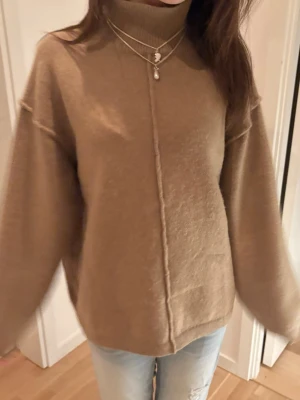 Beige stickad polotröja - Snygg beige stickad polotröja med rak passform och markerad söm framtill. Tröjan har långa ärmar och hög krage, perfekt för lager-på-lager. Mjuk och skön känsla, passar till jeans eller kjol.