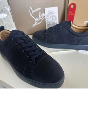 Mörkblå sneakers från Christian Louboutin - Snygga mörkblå sneakers från Christian Louboutin i mocka med matchande mörkblå snörning och diskret logga broderad på hälen. Skorna har en klassisk låg siluett och en svart sula. Perfekta för dig som gillar stilrena och exklusiva detaljer.