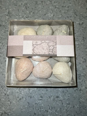 Stenformade ljus i presentask - Säljer ett set med små ljus formade som stenar i olika färger som grå, beige och rosa. Ljusen kommer i en genomskinlig presentask och är perfekta som dekoration eller gåva. Materialet är vax och de har en naturlig, stenlik look.