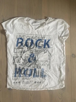 Vit t-shirt Zadig & Voltaire Rock & Roll - Cool vit t-shirt från Zadig & Voltaire med blå text 'ROCK & ROLL' och konsertinspirerat tryck framtill. T-shirten har rund hals, korta ärmar och är gjord i mjuk bomull. Perfekt för dig som gillar rockig stil och statement-plagg.
