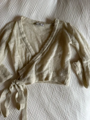 Beige omlottkofta med knytband - Säljer en beige stickad omlottkofta från NAKD. Koftan har långa ärmar, djup V-ringning och knytband i midjan. 