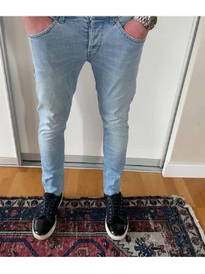 Ljusblå slim fit jeans herr - Säljer ett par ljusblå slim fit jeans med klassisk femficksdesign och smal passform. Jeansen har normal midja, dragkedjegylf och subtila slitningar för en modern look. Perfekta till sneakers och t-shirt för en avslappnad stil.