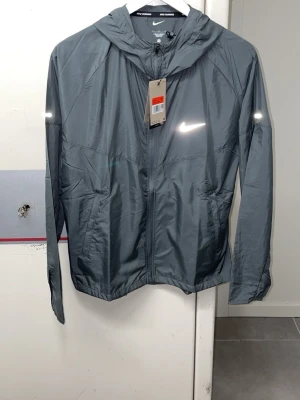 Nike windbreaker miler jacka - Grå Nike jacka, i helt nytt skick med lapparna och allting, Storlek M